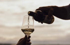 Den Wein genießen, © Weinviertel Tourismus / Sophie Menegaldo Wein wird in ein Glas im Freien eingeschenkt, im Hintergrund eine Landschaft.