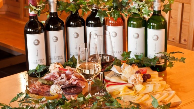 kalte Platten und Weinflaschen, © Vinterra Zöchling Weinflaschen und kalte Platten mit Käse und Wurst auf einem Tisch.