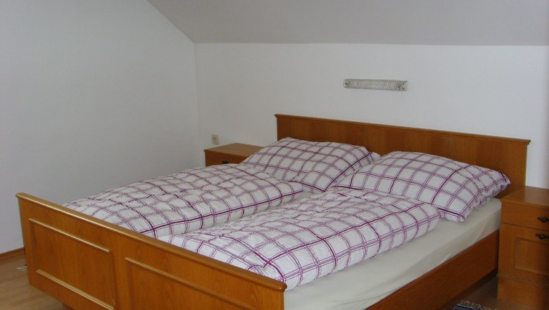 Privatzimmer Eder, © Eder Schlafzimmer mit Holzbett und kariertem Bettzeug.
