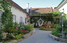 Winzerhof Wurst, © Christoph Wurst Ein idyllischer Innenhof mit Blumenbeeten, einer Hängematte und einem überdachten Sitzbereich.