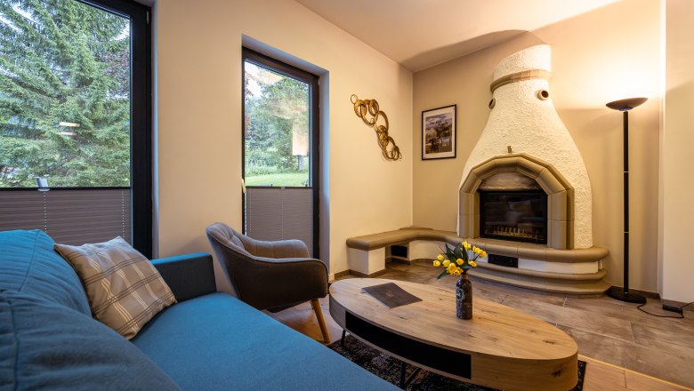 Ötscher Lodge, © Niederösterreich Werbung / Maximilian Pawlikowsky Gemütliches Wohnzimmer mit Kamin, Sofa, Sessel und Couchtisch. Große Fenster mit Blick ins Grüne.