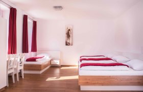 Zimmer, © Familie Gschaider Helles Zimmer mit zwei Betten, roten Vorhängen und einem Bild an der Wand.