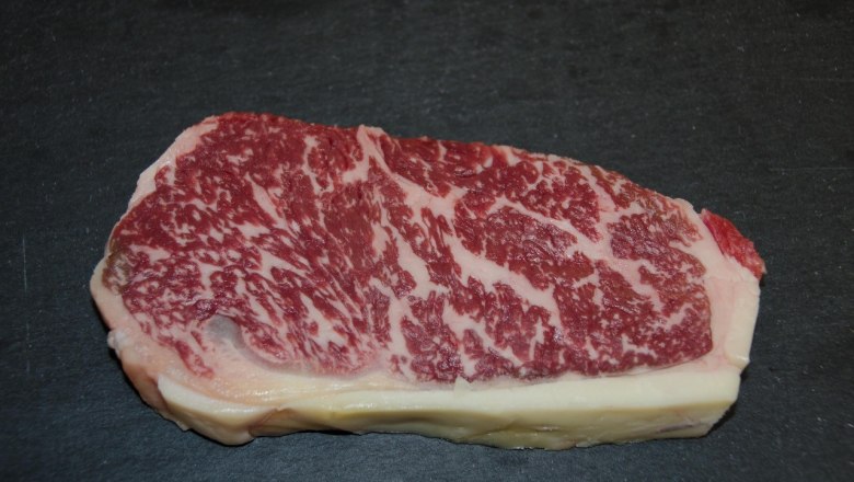 Beiried vom Wagyu Rind, © Matthias Penner Ein Stück Wagyu-Rindfleisch mit starker Marmorierung auf schwarzem Hintergrund.