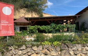 Wein.Keller.Sporr, © Familie Sporr Außenansicht eines Heurigen mit Garten und Werbeschild.