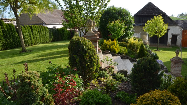 Garten, © Familie Herrmann Ein gepflegter Garten mit Rasen, Büschen und Bäumen, umgeben von Gebäuden im Hintergrund.