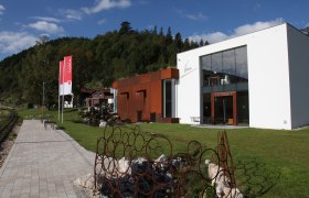 Galerie & Atelier VOKA in Puchberg am Schneeberg, © Voka Moderne Galerie mit Glasfassade und rostigen Metallskulpturen im Grünen.