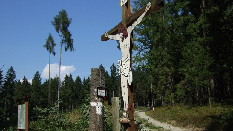 Kastlkreuz am Jakobsweg, © Gemeinde Bergern im Dunkelsteinerwald Ein hölzernes Kruzifix am Waldrand mit einem Weg im Hintergrund.