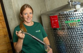 Veronika Pichler, Geschäftsführerin, © spusuwein Eine Frau in einem grünen T-Shirt steht neben einem großen Edelstahltank und hält ein Glas mit einer Flüssigkeit.