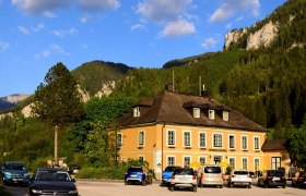 Wirtshaus zum Raxkönig, © Reinhard Maurer Ein gelbes Gebäude vor einer Bergkulisse mit geparkten Autos davor.