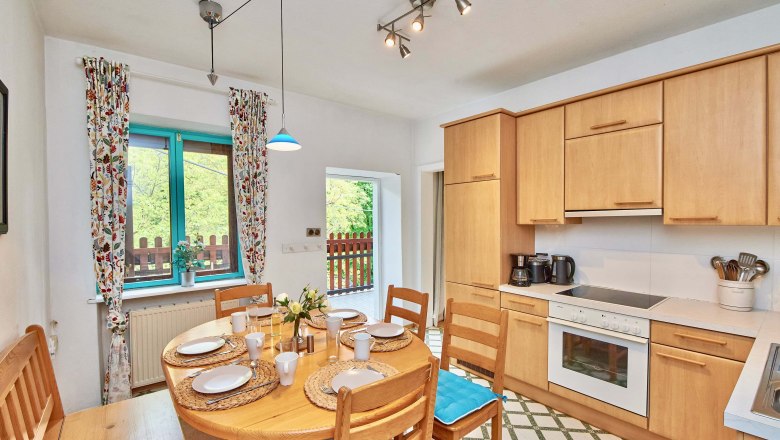 Top 2 - Küche, © VP FeWo OG Gemütliche Küche mit Holzmöbeln, Esstisch und Fenster mit bunten Vorhängen.