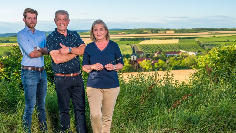 Elfriede, Josef und Martin Heinzl, © Wolfgang Artner Drei Personen stehen in einem Weingarten mit Blick auf eine ländliche Landschaft im Hintergrund.
