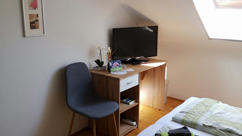 Zimmer 2, © Haselberger Ein gemütliches Zimmer mit einem Bett, einem kleinen Schreibtisch mit Fernseher, einem Stuhl und einem Dachfenster.