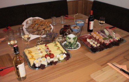 Köstlichkeiten am Weingut, © Familie Schüller Ein gedeckter Tisch mit Käse- und Wurstplatten, Brot, Wein und Gläsern.