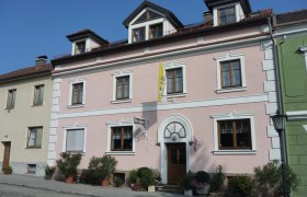 Haus Regina Aussenansicht, © Haus Regina Außenansicht eines rosa Hauses mit weißen Fensterrahmen und einer gelben Fahne.