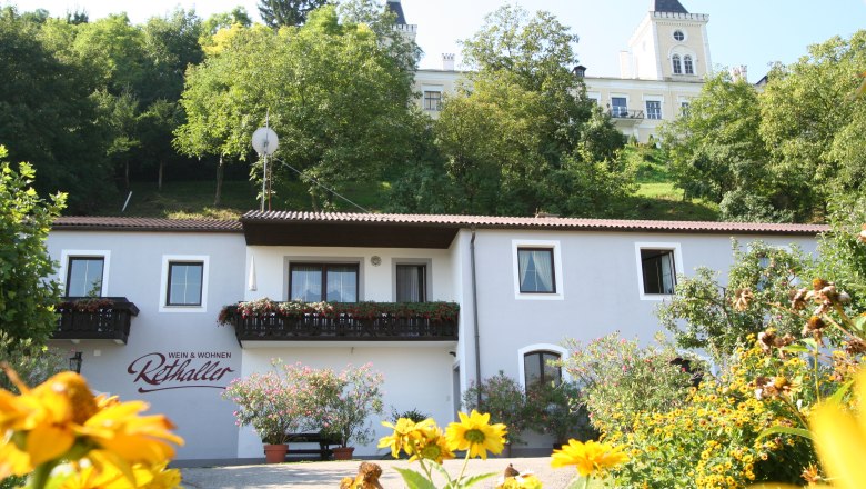 Aussenansicht Fam. Rethaller, © rethaller Außenansicht eines Hauses mit Blumen und einem Gebäude im Hintergrund.