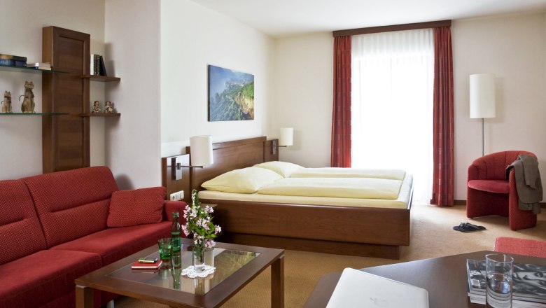 Landgasthof 'Zur Schönen Wienerin', © Engel Gemütliches Hotelzimmer mit Doppelbett, rotem Sofa, Glastisch und Dekorationen.