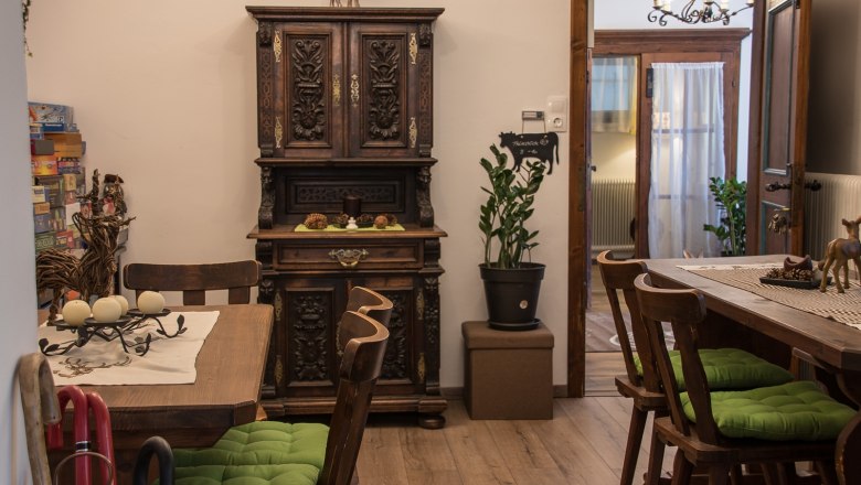 Aufenthaltsraum, © Dirnbauer Gemütlicher Aufenthaltsraum mit Holzmöbeln, grünen Sitzkissen und dekorativem Schrank.