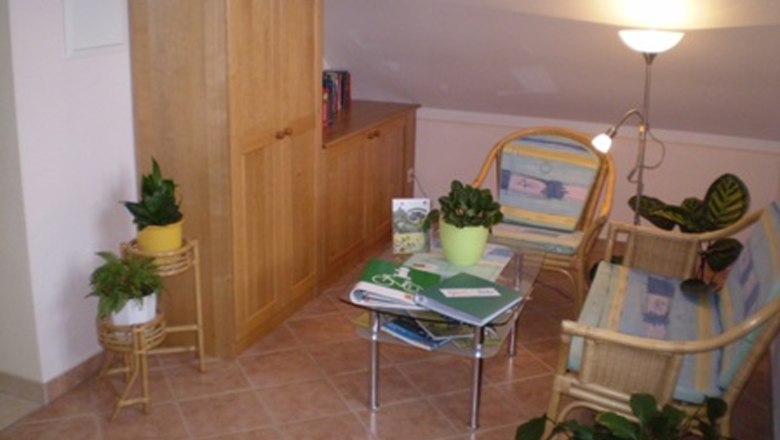 Leseecke, © Gästezimmer Rieder Gemütliche Leseecke mit Rattanmöbeln, Pflanzen und einem kleinen Tisch mit Büchern.