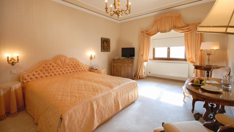 Gästezimmer, © Schwalben in der Lobby Elegantes Gästezimmer mit großem Bett, Kronleuchter und Tisch mit Obst.