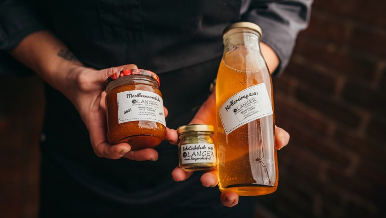 Marmeladen, Sirupe und Chutneys vom Langer, © Niederösterreich Werbung/Daniela Führer Person hält Gläser mit Marillenmarmelade und Hollersirup von Langer.