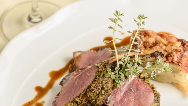 Speisenansicht Hotel-Restaurant Zur Post, © BOW Rita Newman Ein Teller mit Lammkoteletts in Kräuterkruste, Gemüsebeilage und Soße, daneben ein Glas Rotwein.