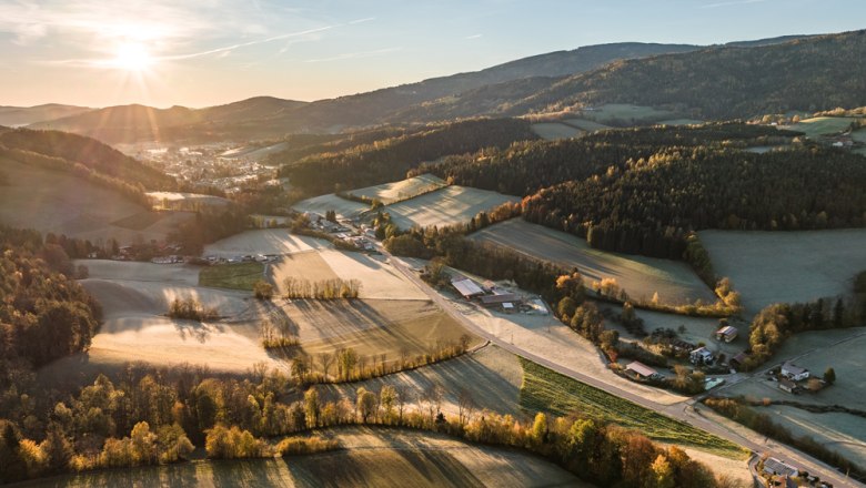 Gemeinde Otterthal, © Wiener Alpen, Christian Kremsl Luftaufnahme einer ländlichen Landschaft bei Sonnenaufgang mit Feldern, Wäldern und vereinzelten Gebäuden.
