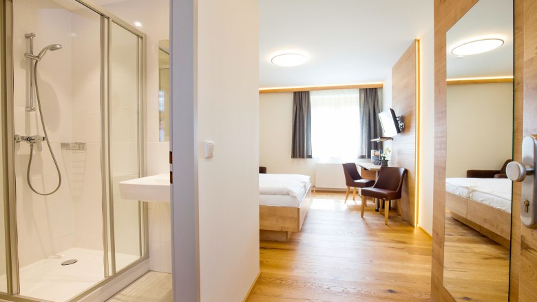 Zimmeransicht, © Hotel Stich Modernes Hotelzimmer mit Bad, Bett, Schreibtisch und Stühlen.