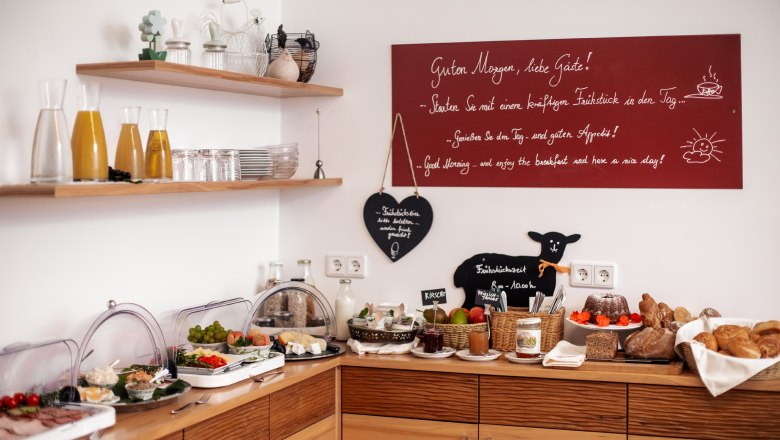 Gästehaus-Winzerhof Bernhard, © Jolly Schwarz Frühstücksbuffet mit Saft, Brot, Aufschnitt und Obst in einem gemütlichen Raum.