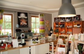 Der Hofladen, © Weingut Dachauer Innenansicht eines Hofladens mit Regalen voller Weinflaschen und Produkten.