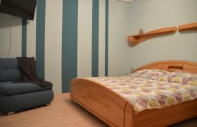 Schlafzimmer, © Eva Stuhr Schlafzimmer mit gestreifter Wand, Holzbett und Sofa.