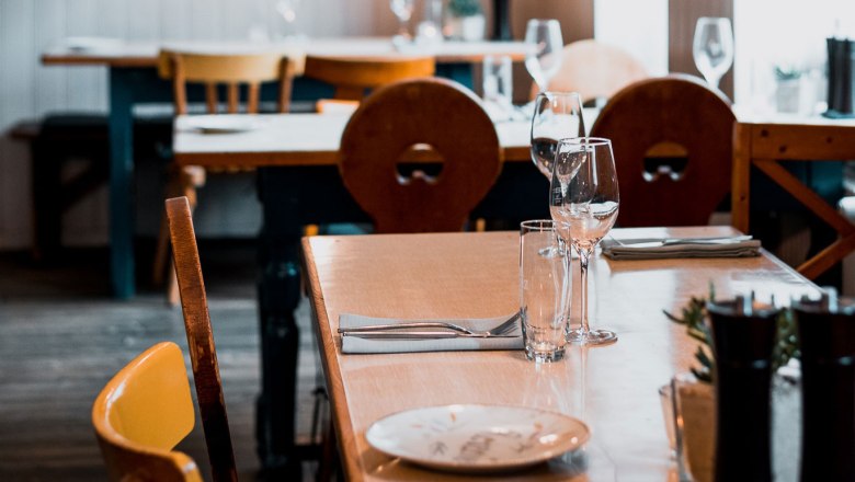 Urbanes Wirtshausflair, © Vinzenz Pauli/Philip Hinteregger Ein gedeckter Tisch in einem gemütlichen Restaurant mit Holzmöbeln und Weingläsern.