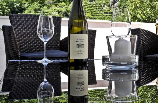 Terrasse, © Gästehaus Johanna Weinflasche und Gläser auf einem Tisch mit Blick auf Weinberge.