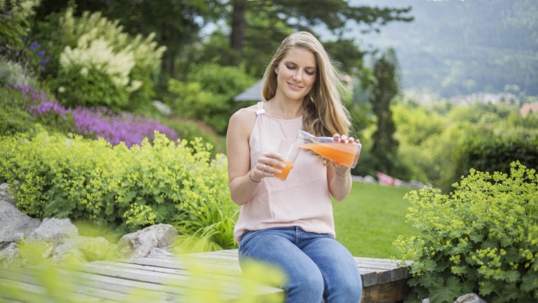 Ausruhen im Alpengarten., © Patrick Haberler Frau sitzt im Garten und gießt Saft in ein Glas.