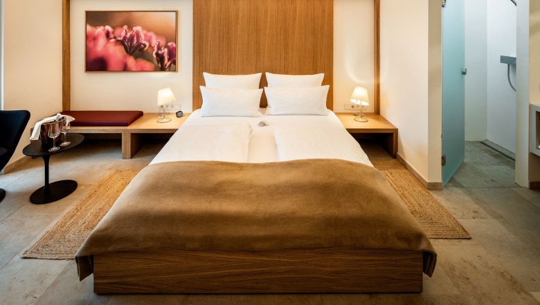 Gästehaus Flora, © Herbert Lehmann Modern eingerichtetes Hotelzimmer mit Doppelbett, Nachttischen, Lampen und einem Bild an der Wand.