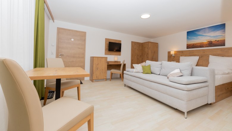 Schlafzimmer mit Schlafsofa, © Schönfelderhof Modernes Schlafzimmer mit Schlafsofa, Tisch und Stühlen, Holzmöbeln und Landschaftsbild an der Wand.