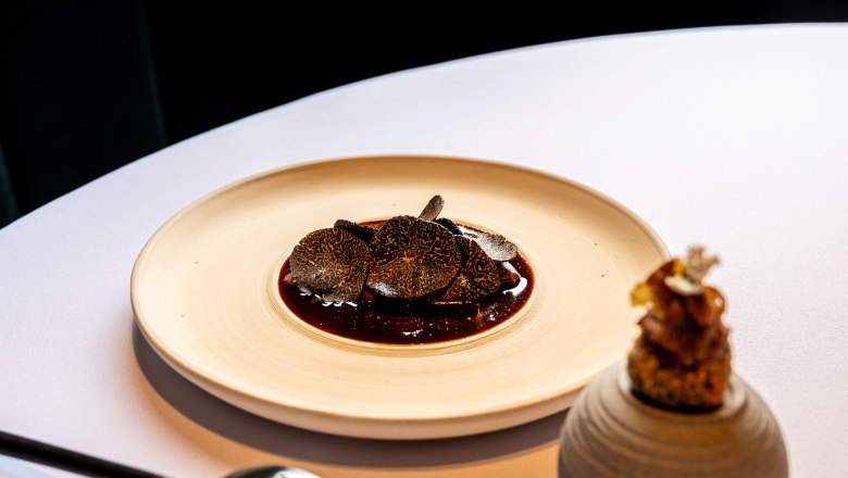 Taube, © Claus Kadrnoschka Ein Gourmetgericht mit Trüffelscheiben auf einem Teller, daneben ein dekoratives Element.