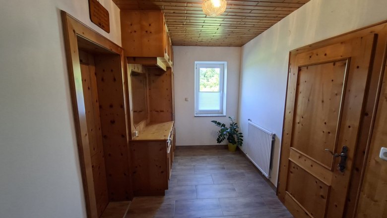 Vorraum, © Ferienwohnung Penz Stolzenthal, Fotograf Hermine Penz Ein schmaler Flur mit Holzmöbeln, einer Pflanze und einem Fenster mit Blick nach draußen.