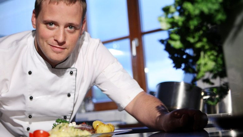 Hochgenuss am Königsberg, © weinfranz.at Ein Koch in weißer Uniform präsentiert ein Gericht in einer Küche.