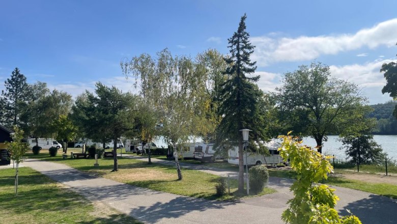 sonnige Stellplätze, © Camping Marbach Campingplatz mit Wohnmobilen und Bäumen am Seeufer bei sonnigem Wetter.