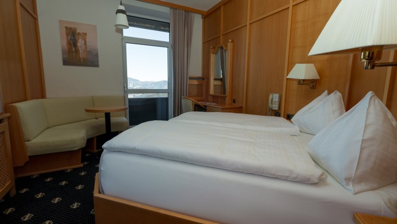 Doppelzimmer, © Sporthotel Semmering Ein gemütliches Doppelzimmer mit Holzmöbeln, einem Doppelbett, einer Sitzecke und einem Balkon mit Bergblick.