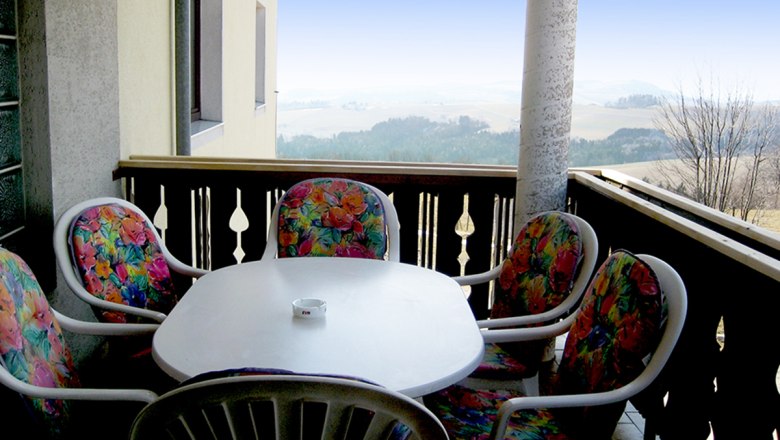 Balkon, © Anke Spreitzer Balkon mit Tisch und bunten Stühlen, Aussicht auf Landschaft.