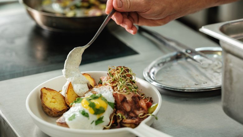 Wein.Restaurant Neustifter, © Weinviertel Tourismus / Michael Reidinger Ein Teller mit gebratenen Kartoffeln, Spiegelei und Sauce wird in einer Küche angerichtet.