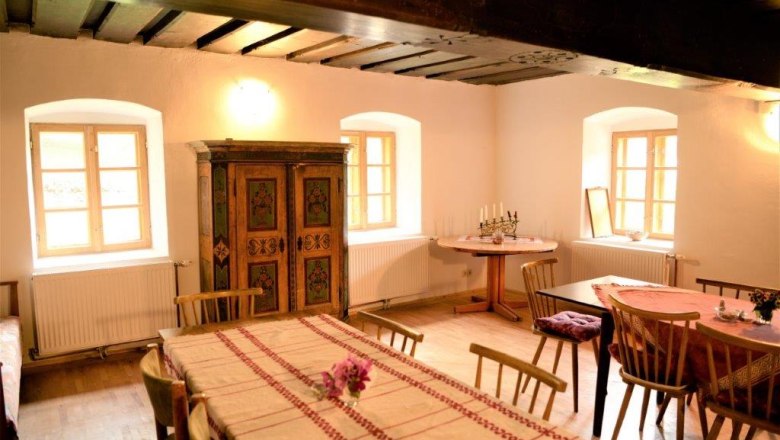 Stube - Mariahaus, © Martina Heilingsetzer Gemütliche Stube mit Holzmöbeln, Tischdecken und einem bemalten Schrank.