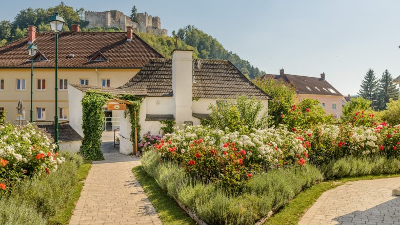 Rosengarten Kirchschlag, © Im Auftrag von Newman& Co fotografie& bildkonzept KG Ein gepflegter Rosengarten mit roten und weißen Rosen, im Hintergrund eine Burg auf einem Hügel.