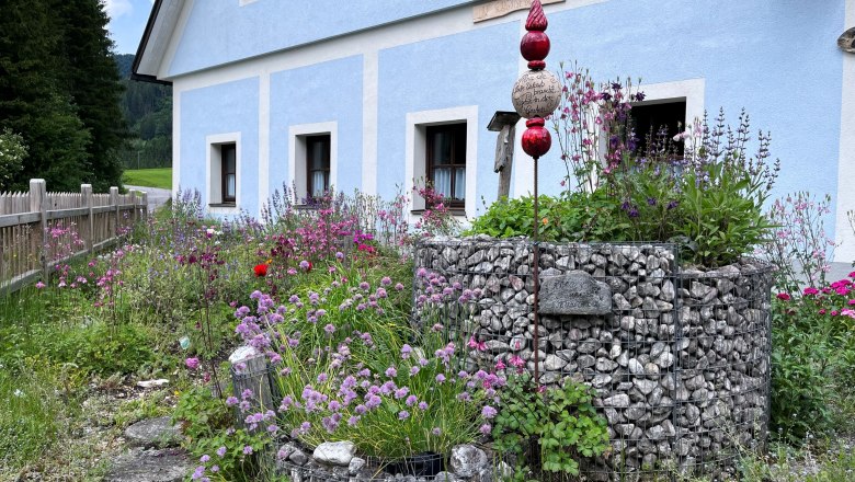 Kräutergarten Kanlehen, © "Natur im Garten" Ein blauer Landhausstilbau mit einem bunten Kräutergarten im Vordergrund.