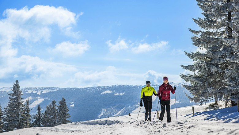 Wechsel-Panoramaloipe, © L&WSV Kirchberg/www.fueloep.com Zwei Langläufer auf einer schneebedeckten Loipe in einer winterlichen Berglandschaft.