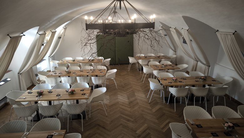 Wappensaal im das Freiherr, © Markus Jokesz Eleganter Saal mit Holztischen, Parkettboden, weißen Stühlen und eisnerner Kronleuchter.