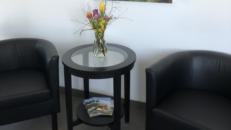 Bernstein Motel, © Bernstein Motel Zwei schwarze Sessel und ein runder Tisch mit Blumen in einem Raum. An der Wand hängt ein abstraktes Gemälde mit Fuchs-Motiv.