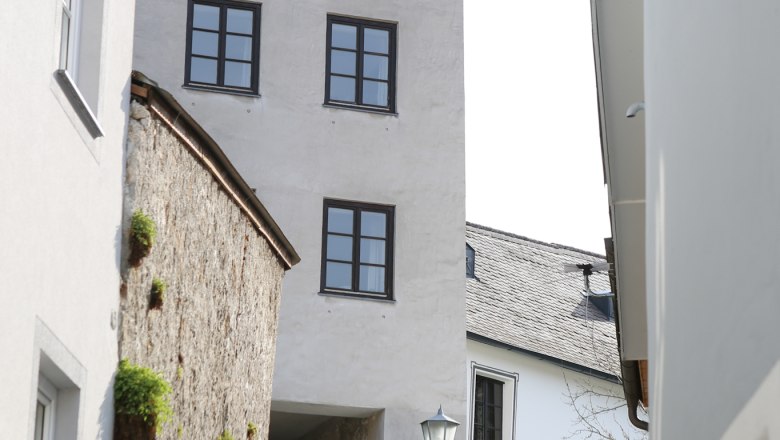 Burgerhoftor, © schwarz-koenig.at Zwei Personen gehen eine gepflasterte Gasse entlang, vorbei an einem historischen Turm mit mehreren Fenstern.