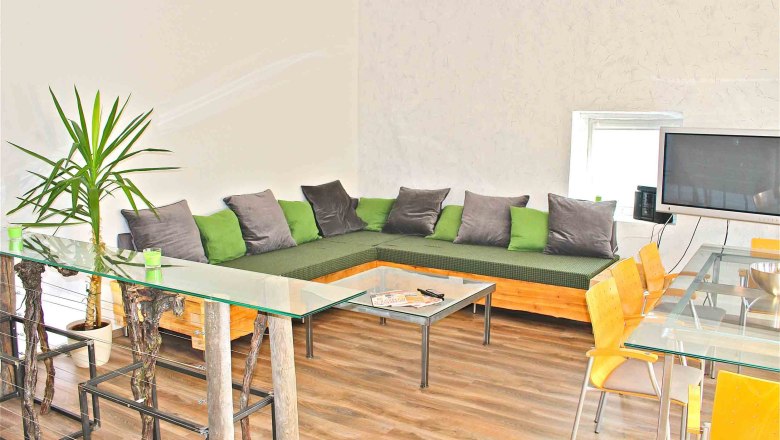 ferien-wohnen, © Frau Lendl Modernes Wohnzimmer mit Ecksofa, Glastisch und Fernseher.